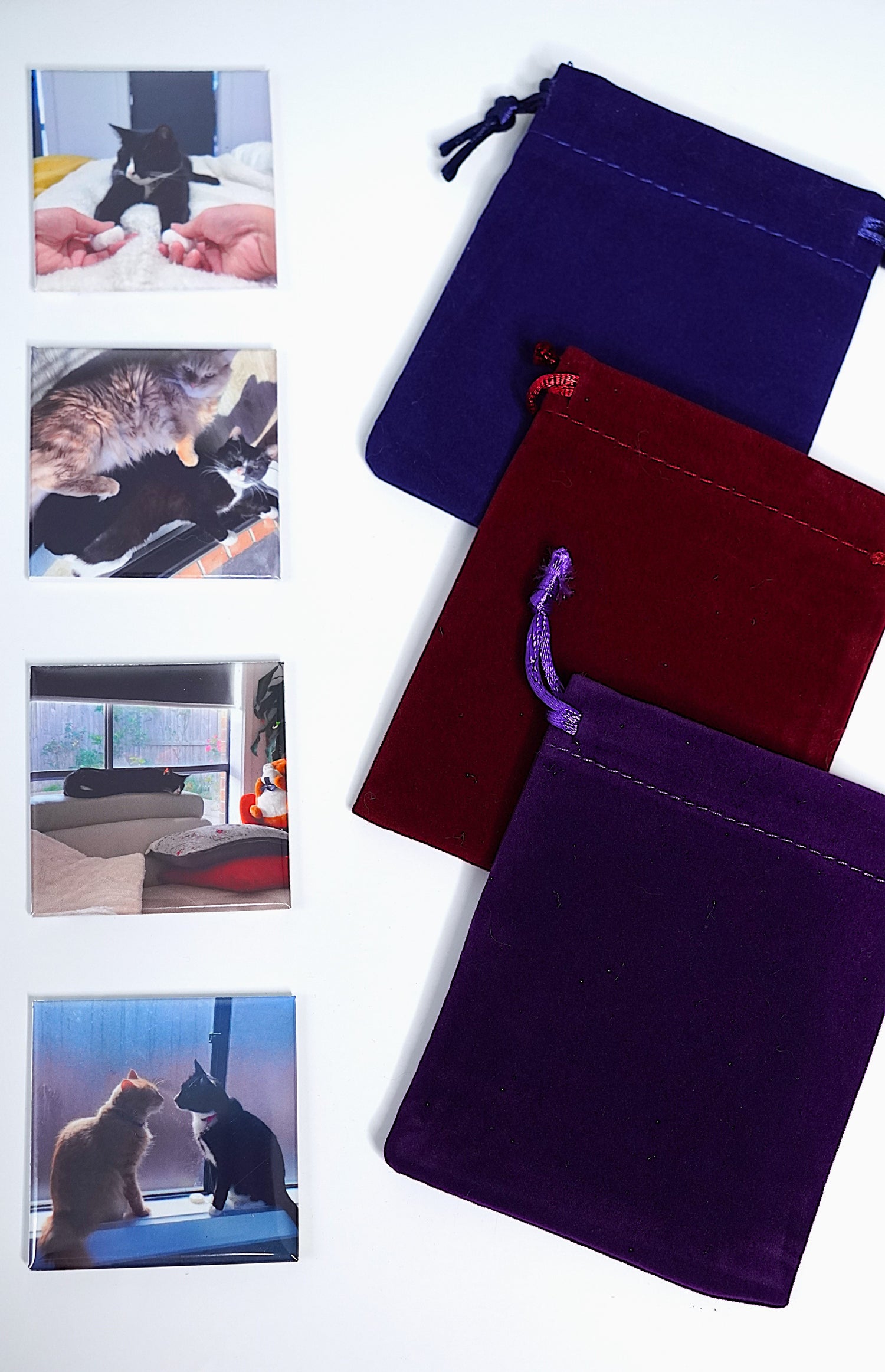 Three velvet bags in purple, red, and blue with cat-themed fridge magnets on a white background for collection