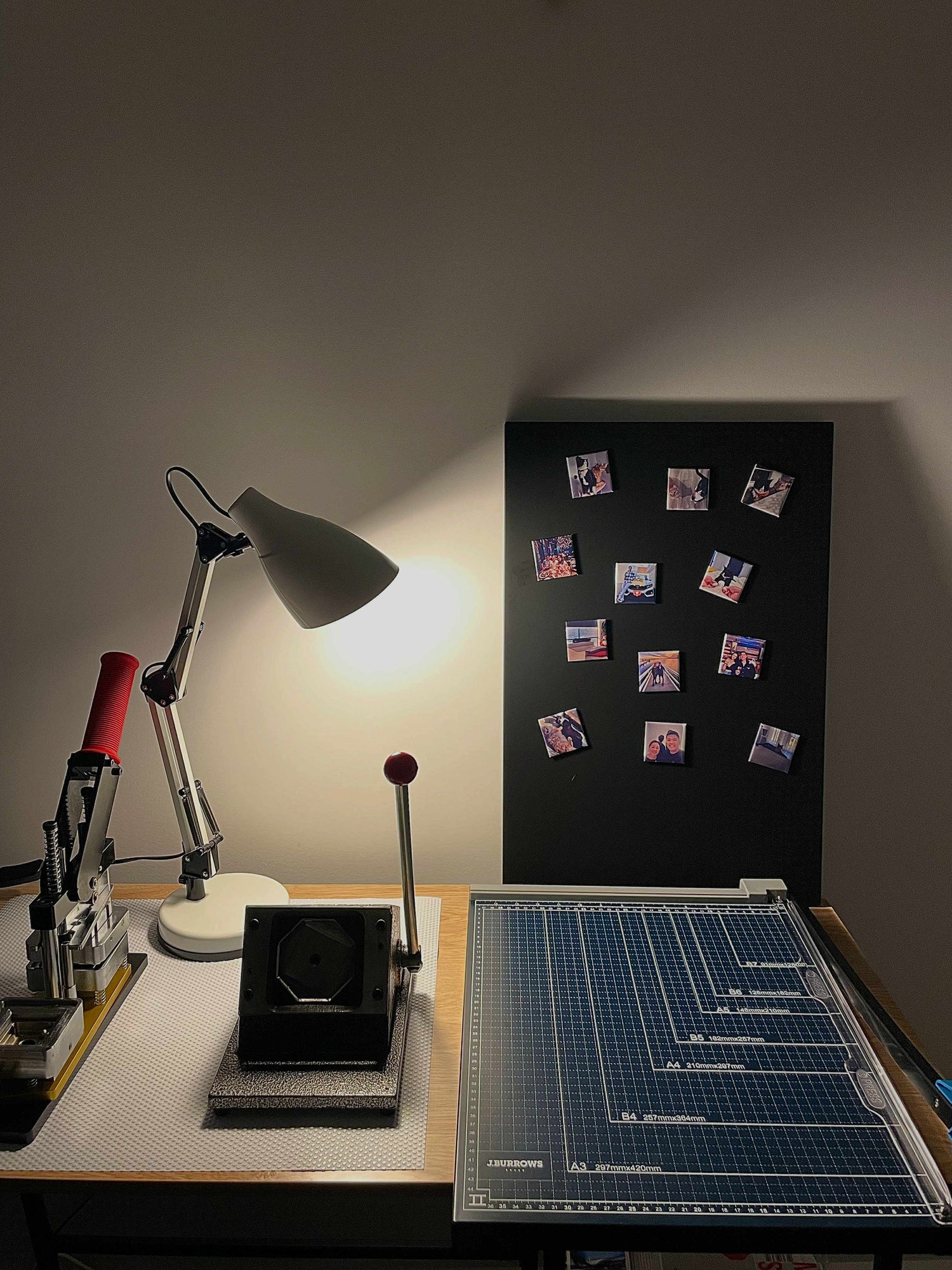 Workstation with a lamp, cutting mat, and small photos on a black board displaying personalised photo fridge magnets Australia.