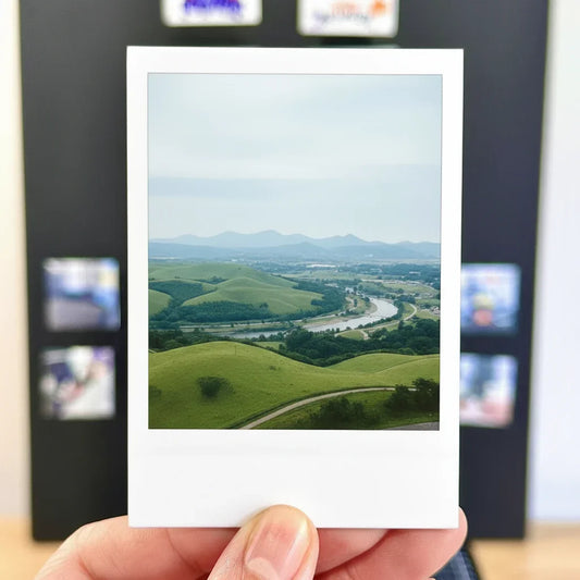 Hand holding a photo magnets of a scenic landscape with green hills and a river retro print fridge magnet decor